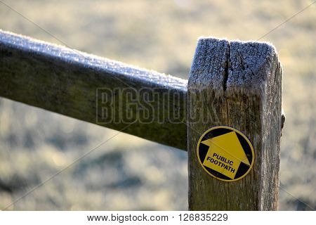 Yellow footpath arrow on oak fence post