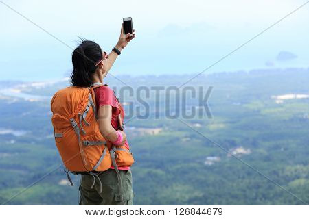 young woman hiker use smartphone taking photo on seaside mountain top