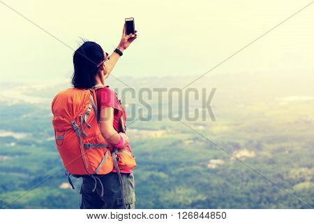 young woman hiker use smartphone taking photo on seaside mountain top
