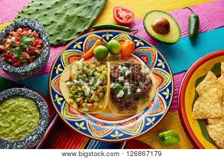 Mexican platillo tacos of barbacoa and vegetarian with sauces and colorful table