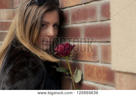 Beautiful girl with a mysterious smile holding a red rose in his hand.