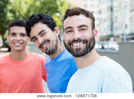 Laughing caucasian man with beard with two friends in the city with buildings and park in the background