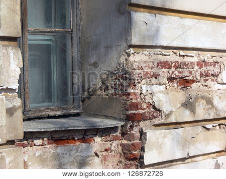 Old window in dilapidated stucco wall of building with red bricks in deep fissures
