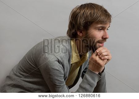 Young man sitting and thinking about his succes, over  grey backfround