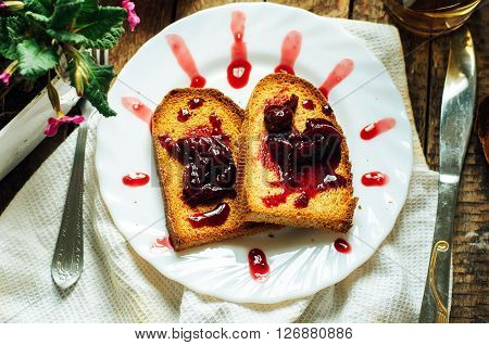 Toast with jam and cup of tea on old wooden table. Delicious toast with jam on table close-up. Fresh cherry jam with toast for breakfast on rustic wooden background. Sweet cherry jam on toast.