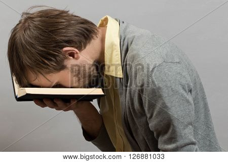 man tired of an uninteresting book against grey wall background