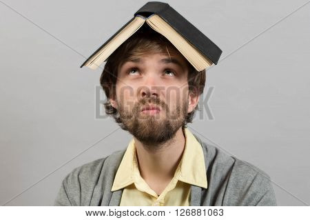 Guy with book on head thinking over grey background