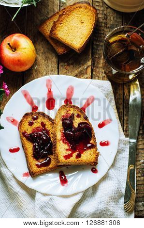 Toast with jam and cup of tea on old wooden table. Delicious toast with jam on table close-up. Fresh cherry jam with toast for breakfast on rustic wooden background. Sweet cherry jam on toast.
