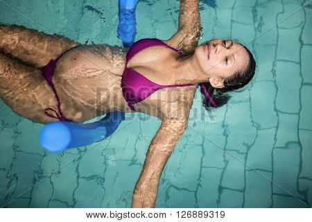 Pregnant woman with foam roller in the pool