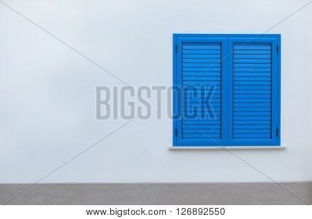 Window with blue shutters on a white wall. Window with closed shutters. Blue window in the wall of the house.