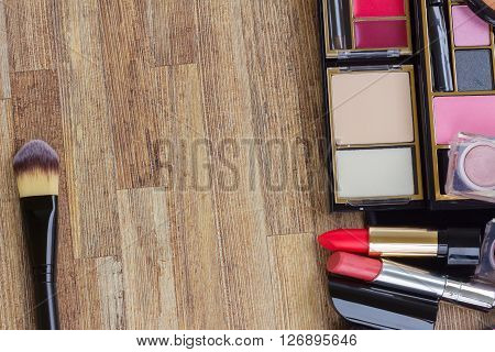 Frame of  brushes, lipsticks, maskara, eye shadows and  powder on wooden desktop, top view