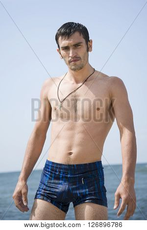 Brutal man all wet came from the water. A man stands on the shore of the warm sea.