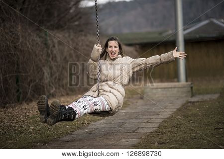 Young woman enjoying life having fun outside in a park on a swing laughing with enjoyment as she flies through the air with one arm wide open.