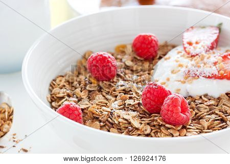 Homemade oat meal granola or muesli with fresh summer fruits - raspberry and strawberry with yogurt in a white bowl on a table for breakfast closeup selective focus