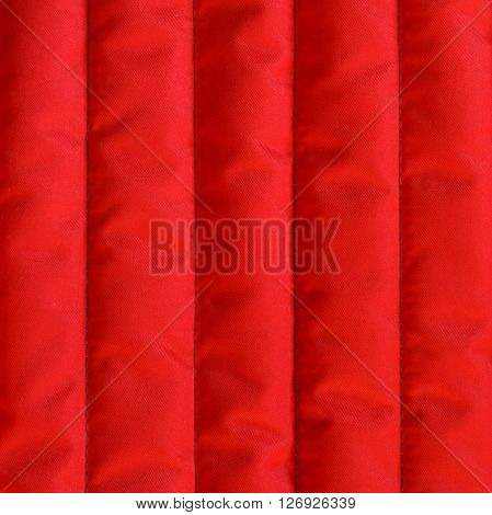 Red quilted textiles with insulation texture. Vertical stripes. Close up fragment of the top view.