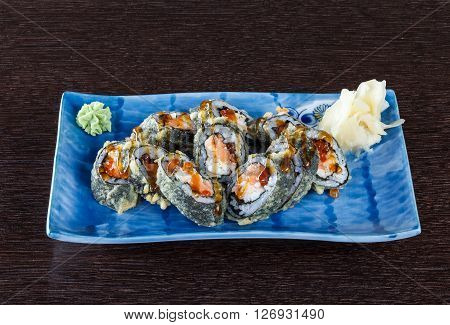 Sushi rolls on a plate with flying fish roe and tuna on dark brown wooden table. Side view.