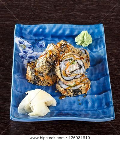 Sushi rolls on a plate with flying fish roe on dark brown wooden table. Side view.
