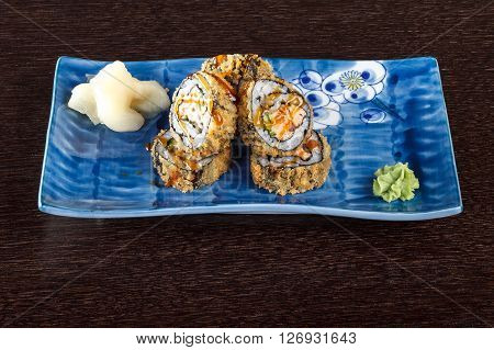 Sushi rolls on a plate with flying fish roe on dark brown wooden table. Side view.