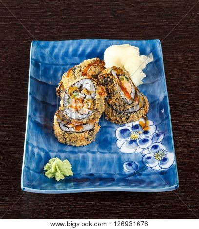 Sushi rolls on a plate with flying fish roe on dark brown wooden table. Side view.