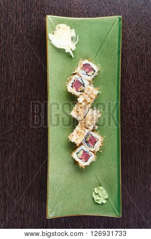 Sushi rolls on a plate with flying fish roe on dark brown wooden table. Side view.