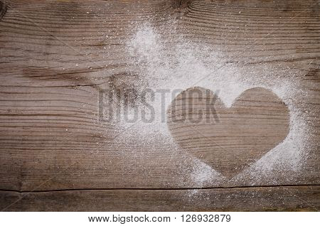 mark in the shape of a heart with powdered sugar on wooden background