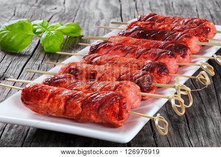Grilled sausages on skewers on a white dish with mustard in a gravy boat on an old rustic table studio lights close-up full focus