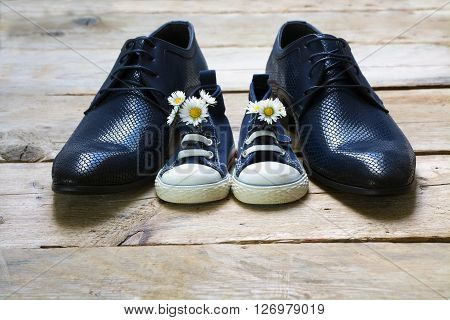 father's day kids sneakers with a bouquet of daisies standing between daddy's black men shoes on rustic gray wood copy space