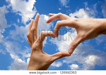Hands with heart shape on the blue sky with clouds.