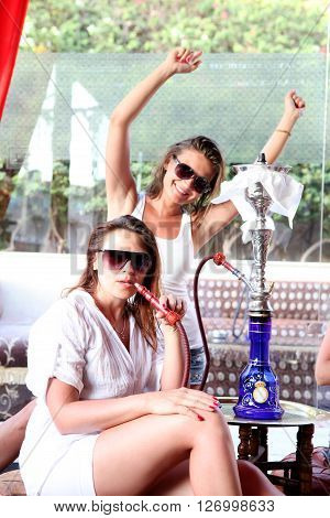Two beautiful happy girls in sunglasses smoking a hookah on vacation