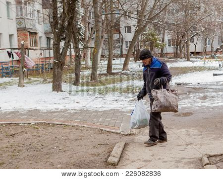 Homeless Old Man With His Bag And Baggage On A Street.
