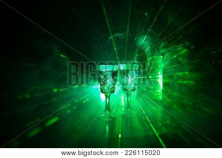 Two Glasses Of Vodka With Bottle On Dark Foggy Club Style Background With Glowing Lights (laser, Sto