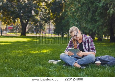 Young Smiling Woman Sitting Outdoors On Grass With Digital Tablet, Typing, Surfing Internet, Prepari