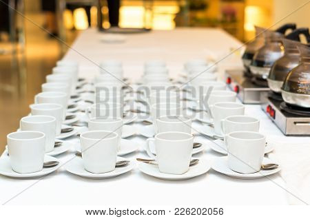 Many Rows Of White Coffee Cup With Saucer And Teaspoon On Table And Coffee Maker Background