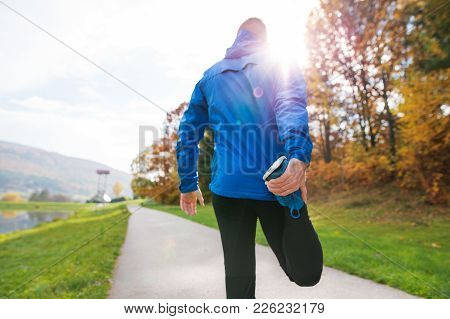 Young Runner In Blue Jacket Outside In Colorful Sunny Autumn Nature Standing On An Asphalt Path, Str