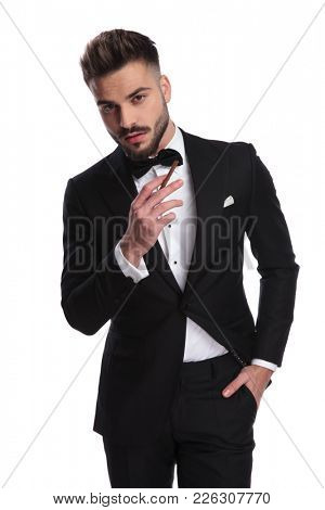 portrait of an elegant man in tuxedo smoking cigarette on white background