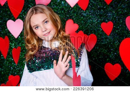 Happy pre-teen girl poses surrounded by little hearts over lawny background. First love. Valentine's Day.