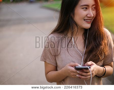 Happy Smiling Young Asian Woman Listens To Music In Headphone And Using Smartphone Searching For Soc