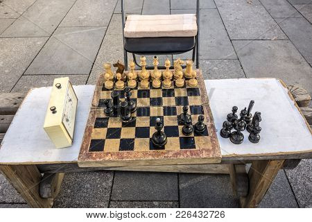 Old Wooden Chessboard, Shabby Wooden Chess Pieces And A Chess Clock Are Located On A Homemade Table 