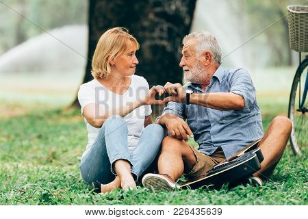 Senior Couple In Love Show Hand Made Heart Shaped Icon Sitting On Grass In The Park