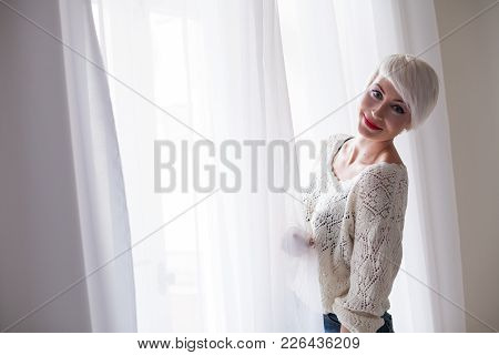 Blonde With Short Hair Stands At The Window Of The Hotel