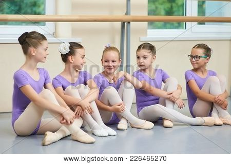 Young Beautiful Ballerinas Talking In Ballet Studio. Group Of Little Ballet Dancers Sitting On The F