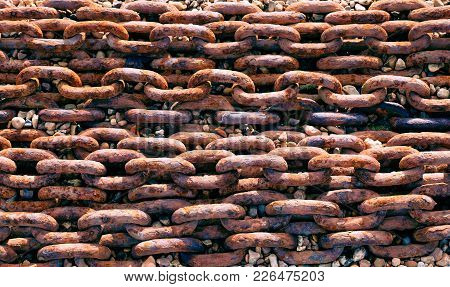 Lines Of Rusted Large Metal Chain On A Stony Beack