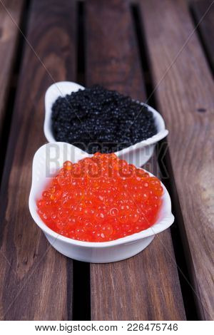 black sturgeon hausen caviar with red salmon caviar in white bowls on wooden background