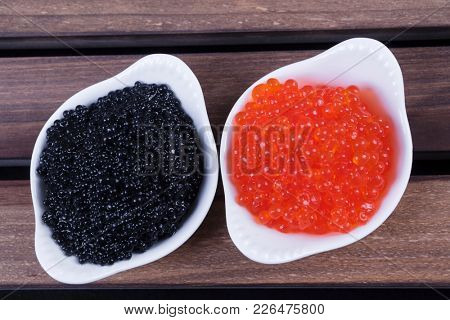 black sturgeon hausen caviar with red salmon caviar in white bowls on wooden background