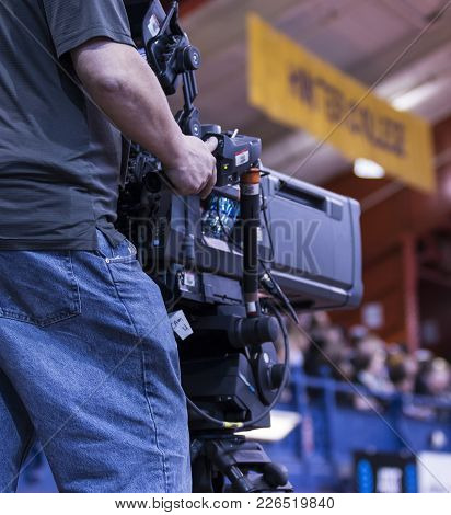 View From Behind Of A Cameraman Is Broadcasting From An Indoor Areana.