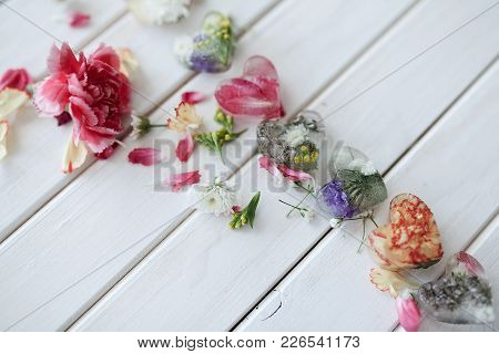 Petals And Ice Hearts With Flowers Inside On A White Wooden Background