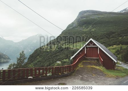 Red garage in norwegian Geiranger village in western Norway. Sunnylvsfjorden fjord from high viewpoint on background