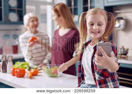 Peace At Home. Pleasant Young Woman Sitting On The Kitchen Counter And Taking Selfies Of Herself And