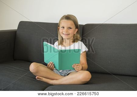 Young Sweet And Happy Little Girl 6 Or 7 Years Old Sitting On Home Living Room Sofa Couch Reading A 