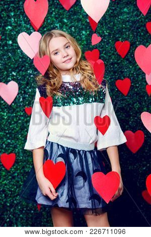 Happy pre-teen girl poses surrounded by little hearts over lawny background. First love. Valentine's Day.
